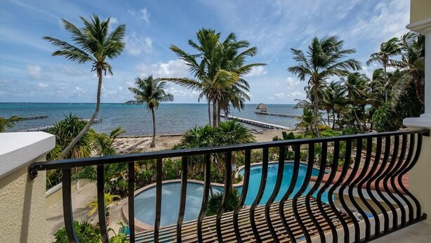 Ein Balkon mit Pool, Palmen und Blick aufs Meer.
