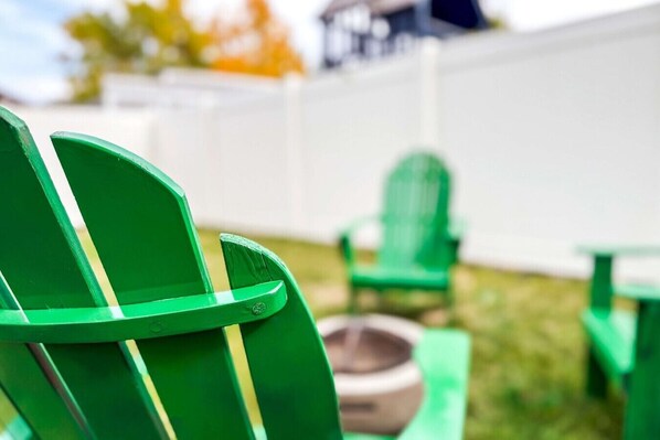 A green chair with a cushion, a green table, and a white fence in the background.