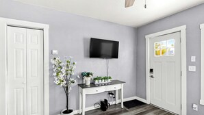 Une pièce avec une porte blanche, un bureau blanc sur lequel est posé un téléviseur à écran plat, une plante en pot et une fenêtre donnant sur un paysage agréable.