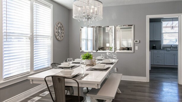 Een eetkamer met een witte tafel gedekt voor vier personen, een kroonluchter en een grote spiegel boven de tafel.