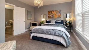 Een slaapkamer met een groot bed, een kroonluchter, een schilderij en een raam met zonwering.