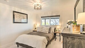 Ein Schlafzimmer mit Bett, Nachttisch, Lampe, Fenster und Kunstwerk.