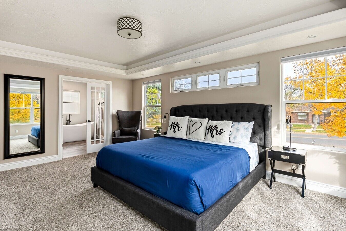 Une chambre à coucher avec un grand lit, une chaise, une table de chevet, une fenêtre donnant sur un beau paysage et une porte menant à une autre pièce.