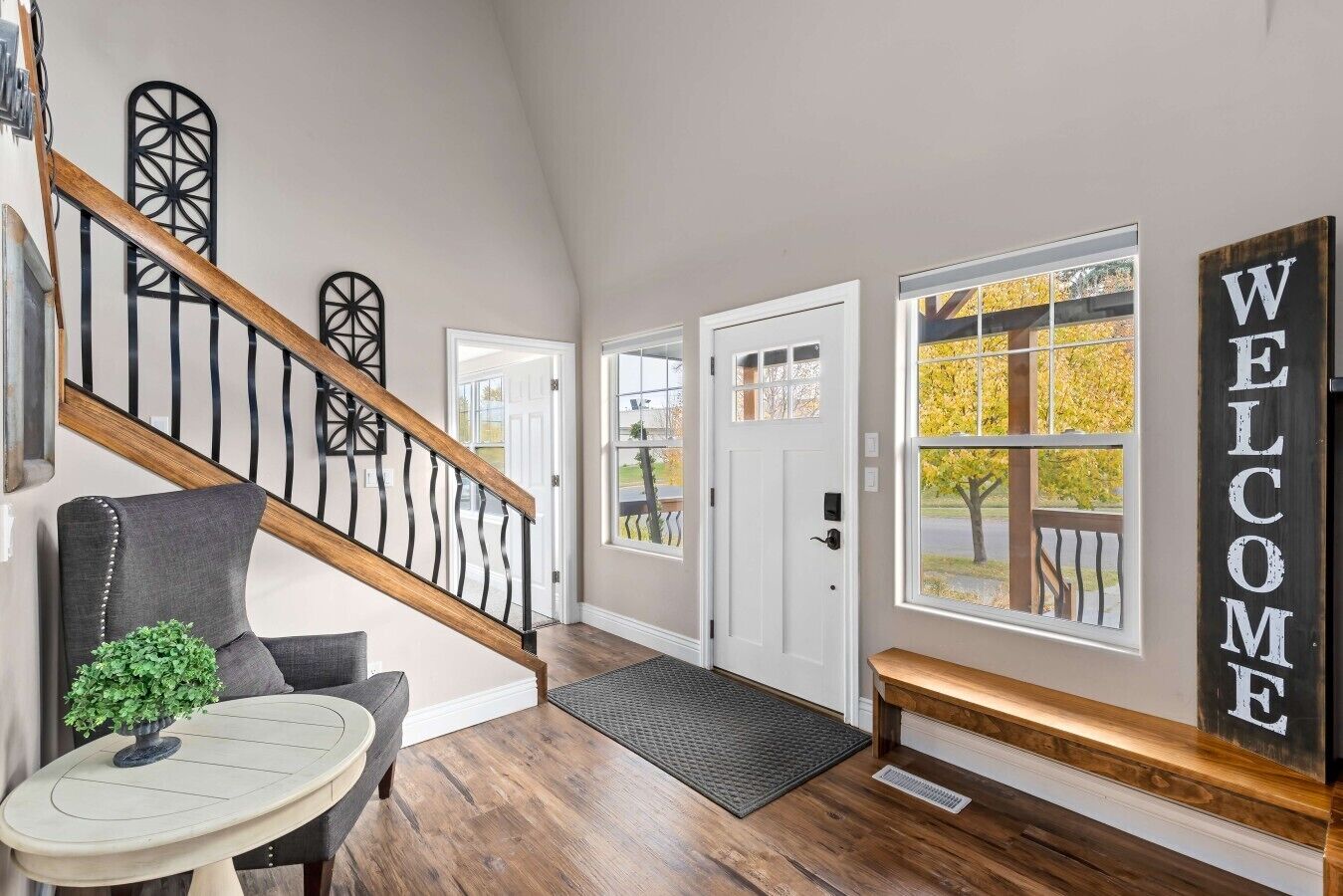 Un intérieur moderne avec un escalier, un banc, une pancarte de bienvenue et une porte dotée d’une fenêtre.