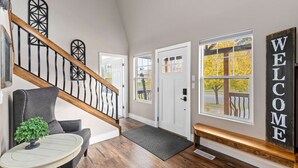 Un interior moderno con una escalera, un banco, un cartel de bienvenida y una puerta con ventana.