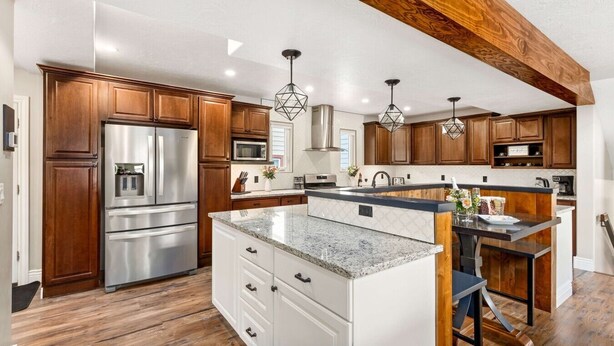 Una cocina moderna con armarios de madera, electrodomésticos de acero inoxidable, una isla de encimera de granito e iluminación colgante.