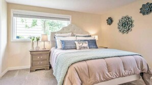 A bedroom with a large bed, a nightstand, a window, and decorative wall art. - Designer Cottage Retreat | Walkable Downtown | W & R (Great Falls)
