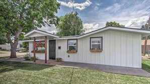 A single-story, white mobile home with a front porch, a small attached garage, and a well-maintained lawn. - Designer Cottage Retreat | Walkable Downtown | W & R (Great Falls)