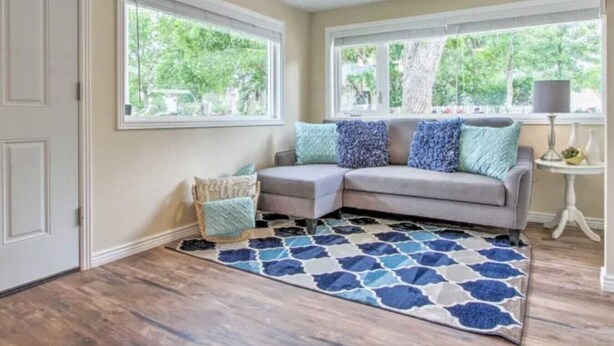 A room with a grey sectional sofa, two windows, a patterned rug, and a small table with a lamp. - Designer Cottage Retreat | Walkable Downtown | W & R (Great Falls)