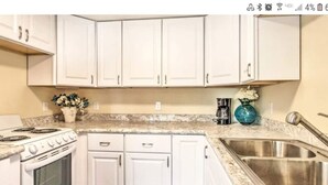 A kitchen with white cabinets, a stove, a sink, and a coffee maker. - Designer Cottage Retreat | Walkable Downtown | W & R (Great Falls)