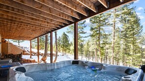 Un jacuzzi en un área exterior cubierta con vistas a un bosque nevado.
