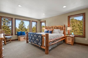 Quarto espaçoso com cama grande, várias janelas e vista para árvores.