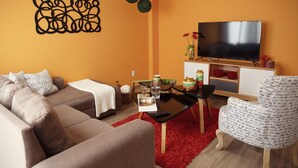 Ein Wohnzimmer mit einer Couch, einem Couchtisch, einem Fernseher und einem gemusterten Sessel.