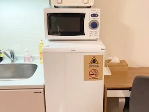 Cocina compacta con microondas, refrigerador miniatura, lavamanos y un cartel de no fumar.
