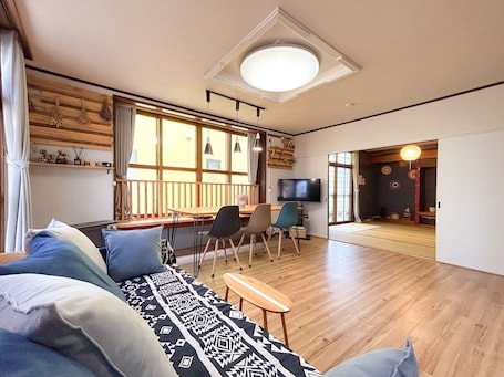 A cozy living room with a sofa, a TV, and a dining area with a wooden table and chairs.