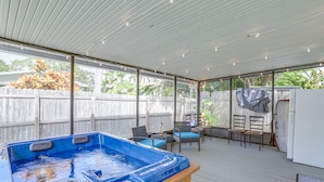 Une terrasse extérieure couverte, dotée d’un jacuzzi, de meubles en osier et offrant une vue sur le jardin.