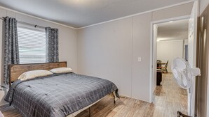 Ein Schlafzimmer mit einem Bett, einem Standventilator und einer Tür zu einem anderen Raum.