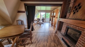A spacious room with a wooden dining table and chairs, a fireplace, and a view of the outdoors through large windows. - Ferienwohnung mit Balkon im Wunderschönen Tecklenburg, Wanderwege (Tecklenburg)