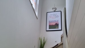 A staircase with a framed poster on the wall, a potted plant, and a window with curtains. - Ferienwohnung mit Balkon im Wunderschönen Tecklenburg, Wanderwege (Tecklenburg)