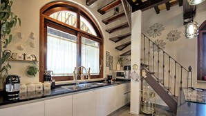 Una cocina moderna con un amplio ventanal, electrodomésticos de acero inoxidable y una escalera decorativa.