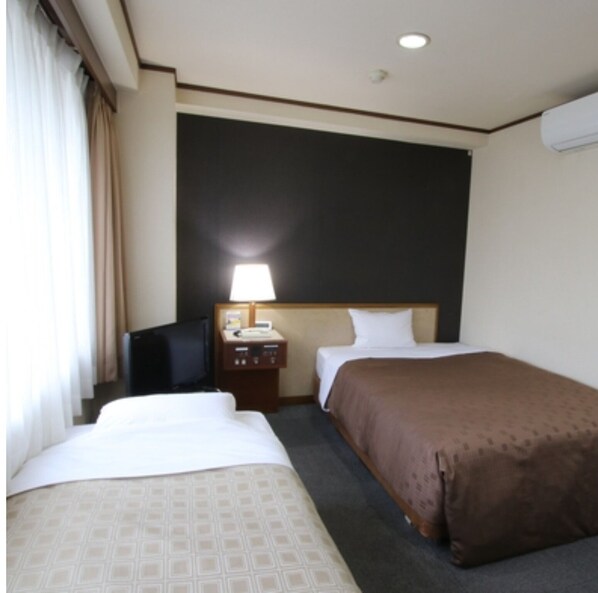 Une chambre d’hôtel avec deux lits, un bureau avec une lampe, une télévision et un appareil de climatisation.