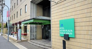 En hotellentrén med ett grönt solskydd och en skylt som visar namnet ”HOTEL ASTON PLAZA SAKAI”.