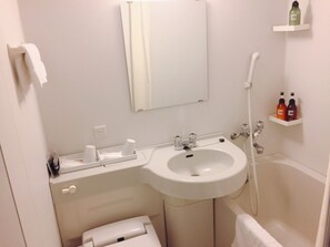 Ein Badezimmer mit Waschbecken, Spiegel, Toilette und Dusche. Auf einem Regal liegen Pflegeprodukte und ein Handtuch hängt an der Wand.