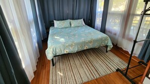 A bedroom with a bed, a wooden floor, a striped rug, and a ceiling light fixture.