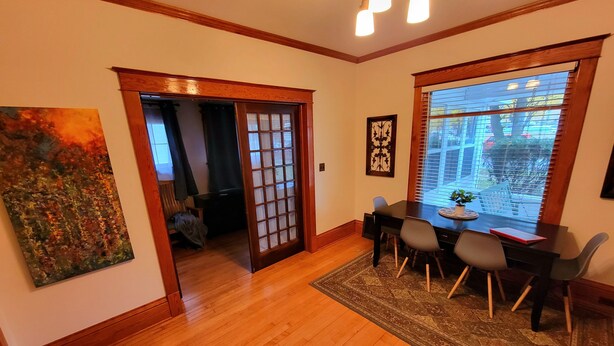A dining area with a wooden floor, a table with chairs, a rug, and a window with blinds.