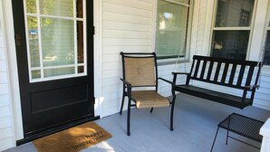 A porch with a black door, a bench, a chair, and a small table.