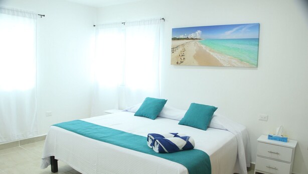 A hotel room with a bed, a nightstand, and a painting of a beach scene. - Casa Sarita (Puerto Morelos)
