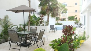 An outdoor patio with a table and chairs, surrounded by plants and a palm tree. - Casa Sarita (Puerto Morelos)