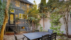 A patio with a wooden table and chairs, a staircase leading to a door, and a wall with climbing plants.