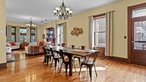 Un salón amplio con comedor, piso de madera y ventanas grandes.
