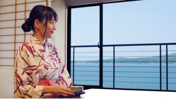 A person seated at a table with a view of the sea through a window with a black railing. - Room is up to youOcean view for 3 people vs |  / Nanao Ishikawa (Nanao)