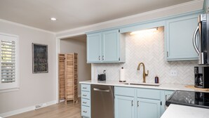 A modern kitchen with light blue cabinets, a stainless steel dishwasher, and a black coffee maker.