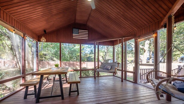 A covered porch with wooden flooring, a table with benches, a swing, and a view of the outdoors.