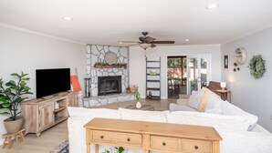 A living room with a stone fireplace, a flat-screen TV, a sofa, a wooden coffee table, and a ceiling fan.