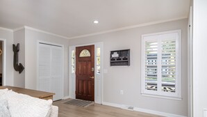A hallway with a wooden door, a white closet, a bench, and a window with shutters.