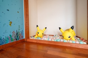 A room with a wooden floor, a wall with a blue ocean-themed mural, and a play area with two Pikachu toys surrounded by colorful balls.