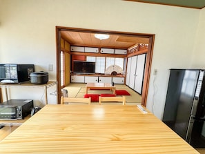 Una habitación de estilo japonés tradicional con suelo de tatami, una mesa de madera baja, un televisor, un ventilador y un refrigerador.