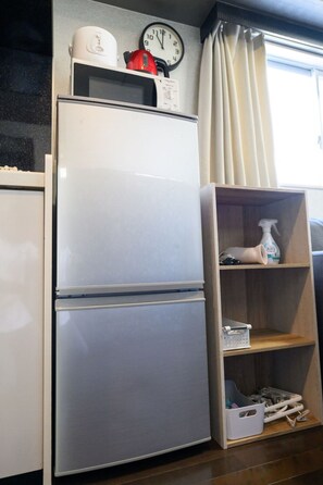 Kitchen area with refrigerator, shelf unit, and window with a view.