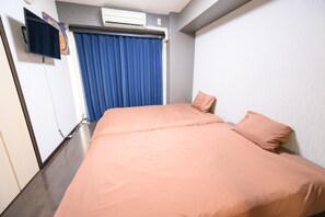 Une chambre d’hôtel avec un lit, un téléviseur à écran plat fixé au mur et une fenêtre avec des rideaux bleus.