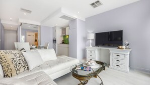 A modern living room with a white sofa, a glass coffee table, and a flat-screen TV on a white cabinet.