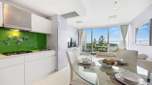 A modern kitchen with white cabinets, a green backsplash, and a dining area with a glass table and white chairs.