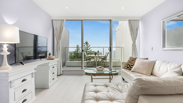 A modern living room with a sofa, a coffee table, a TV, and a balcony with a glass door.