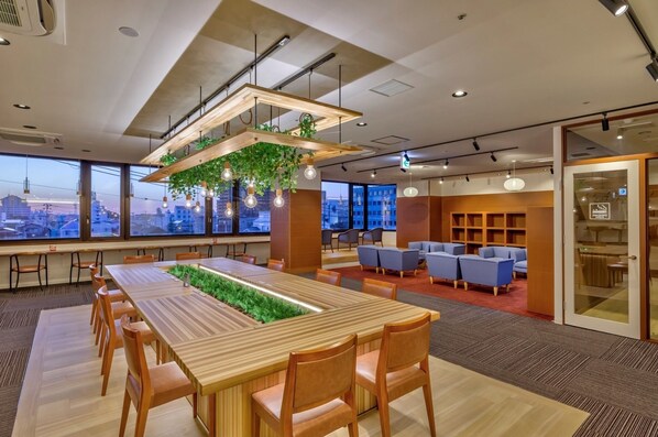 A modern office space with a long wooden table, comfortable seating, and a view of the cityscape through large windows.