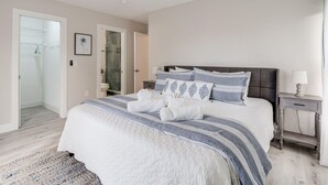 A bedroom with a bed, a nightstand, a ceiling fan, and a bathroom with a glass shower door. - Island Oasis Steps From the Sugar Sand Beach (Fort Myers Beach)