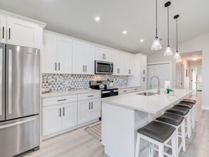 A modern kitchen with white cabinetry, stainless steel appliances, and a central island with bar stools.