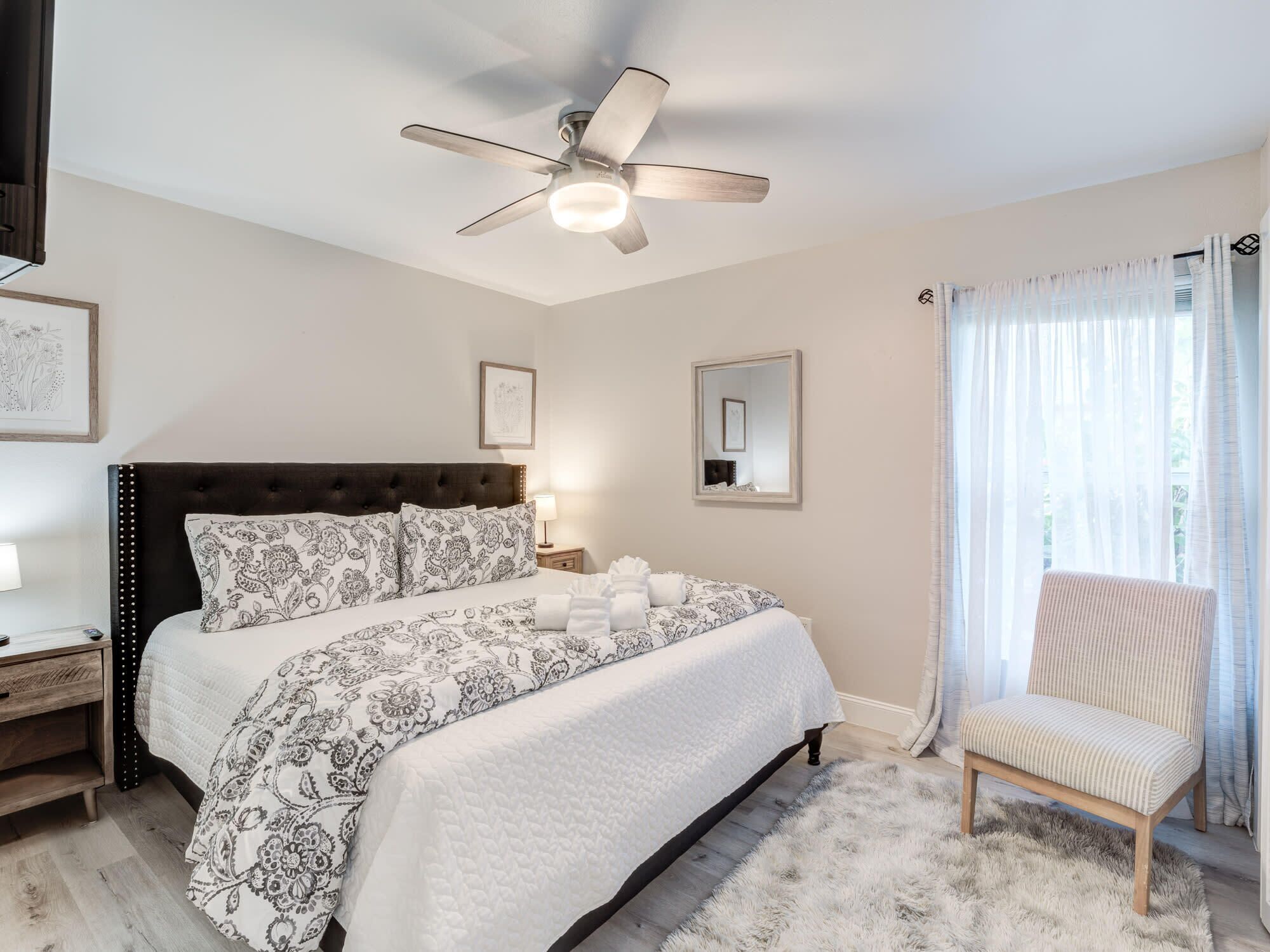 A bedroom with a bed, a chair, a ceiling fan, and a window with curtains.
